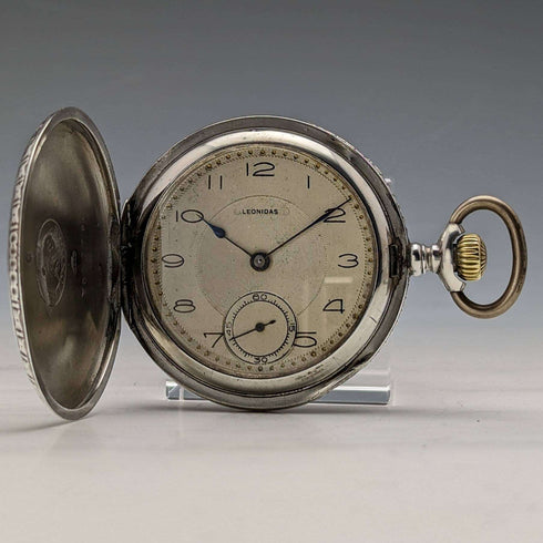 Reloj de bolsillo antiguo Leonidas de fabricación suiza, con caja de plata tipo saboneta grabada con motivos florales, en buen estado de funcionamiento.