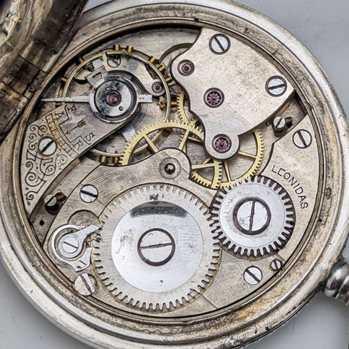 Reloj de bolsillo antiguo Leonidas de fabricación suiza, con caja de plata tipo saboneta grabada con motivos florales, en buen estado de funcionamiento.